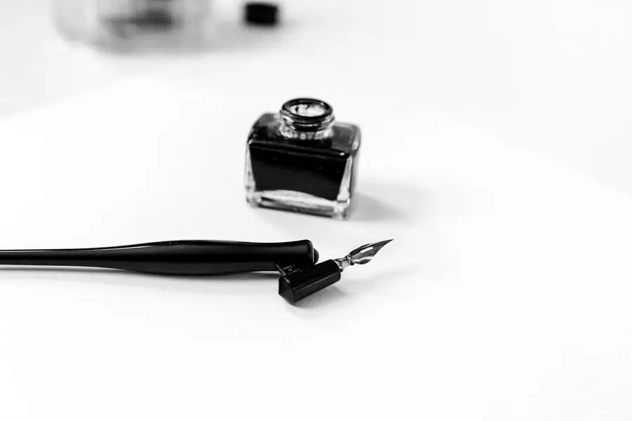 A straight pen holder lying beside a small jar of black ink