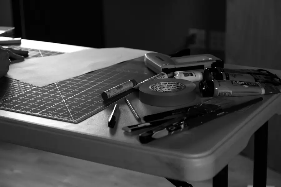 Craft knives, tape and tools on a cutting mat under a warm lamp