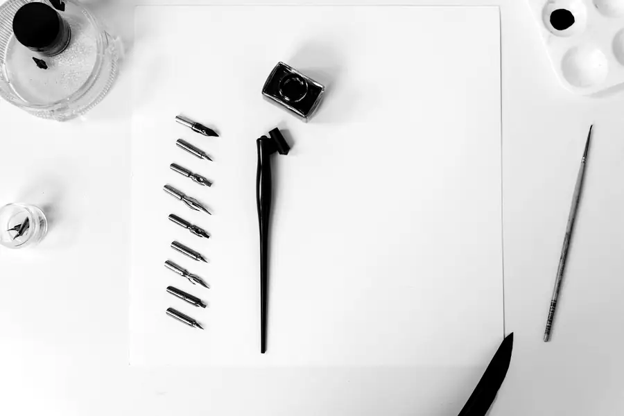 A row of calligraphy nibs beside a pen holder on white paper