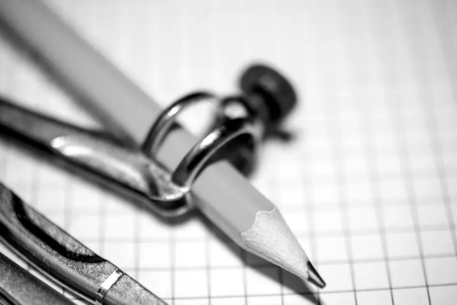 A yellow pencil and a drawing compass lying on graph paper