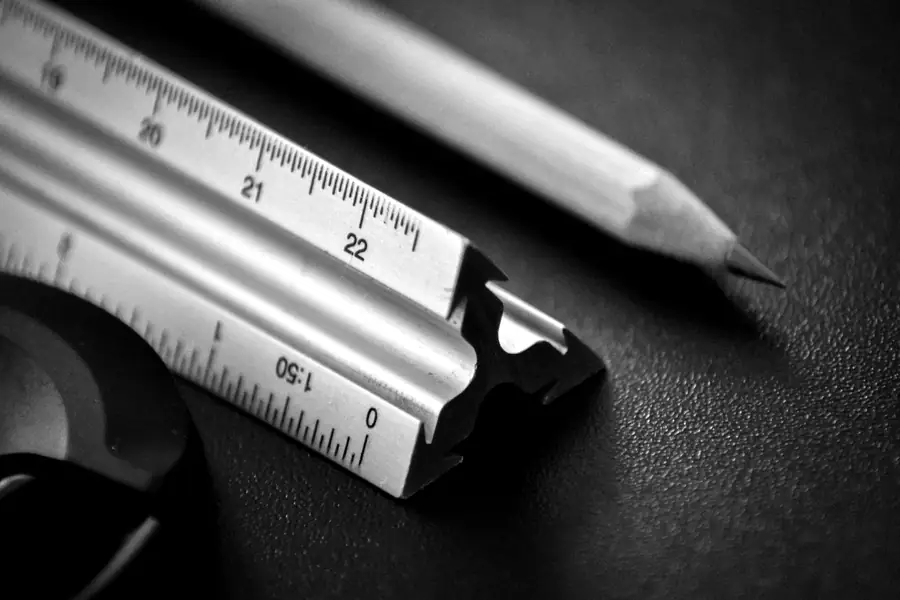 A triangular scale ruler and a sharpened pencil on a dark desk